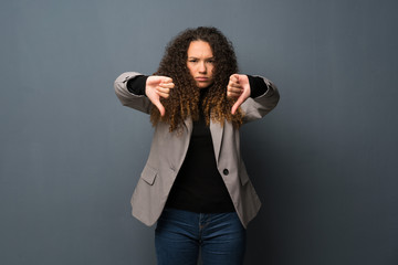 Teenager girl over blue wall showing thumb down