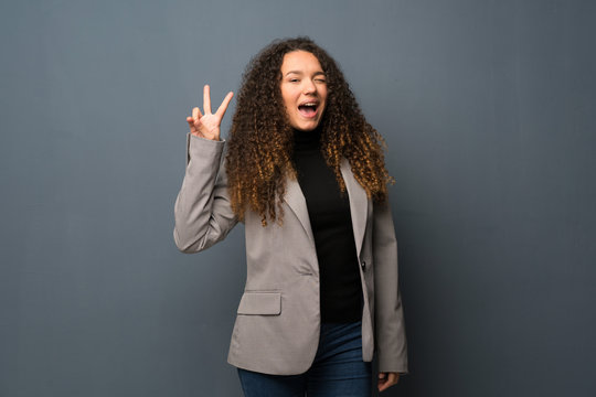 Teenager girl over blue wall smiling and showing victory sign