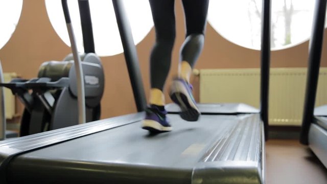 Fitness girl running on treadmill. Woman with muscular legs in gym