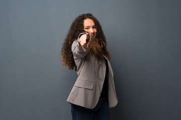 Teenager girl over blue wall points finger at you with a confident expression