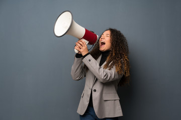 Teenager girl over blue wall shouting through a megaphone