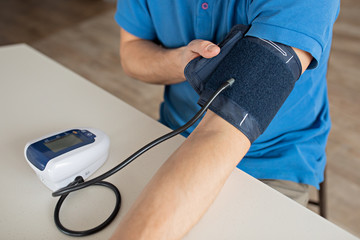 Hypertension concept. Man is measuring blood pressure with monitor in home. Hands close-up