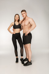 Obraz premium Shirtless athletic man and young woman in black sportswear posing over grey background