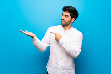 Young man over isolated blue wall holding copyspace imaginary on the palm to insert an ad