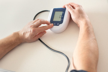 Hypertension concept. Man is measuring blood pressure with monitor in home. Hands close-up