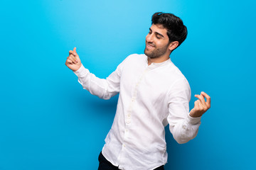 Young man over isolated blue wall enjoy dancing while listening to music at a party