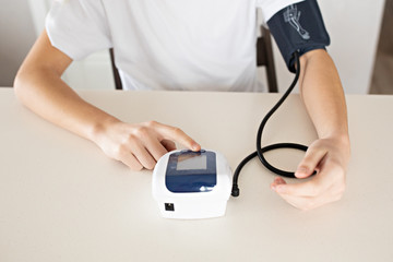 Hypertension concept. Teenager is measuring blood pressure with monitor in home. Hands close-up