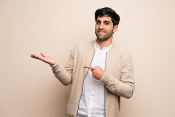 Young man over isolated wall holding copyspace imaginary on the palm to insert an ad