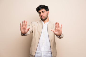 Young man over isolated wall making stop gesture and disappointed