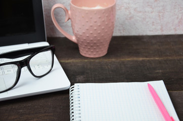Computer image coffee cup resting on a wooden backgroud. desktop, work space of a journalist, blogger, freelancer, office supplies glasses pen, notebook