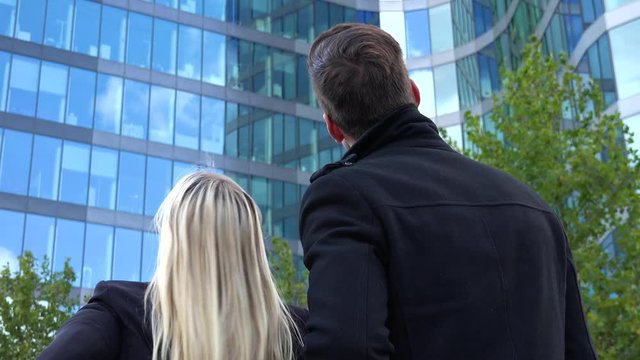 A businessman and a businesswoman look at an office building - view from behind