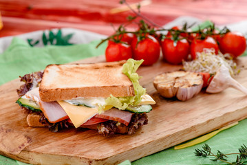 Sandwich with ham, tomatoes, cheese, sauce and lettuce on a wooden board and napkins among vegetables. close up