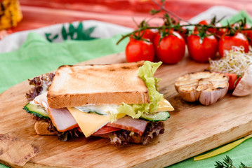 Sandwich with ham, tomatoes, cheese, sauce and lettuce on a wooden board and napkins among vegetables. close up