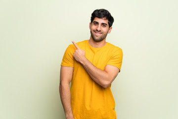 Young man over pink wall pointing to the side to present a product