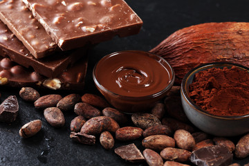 Melting chocolate or melted chocolate with a chocolate swirl and stack, chips and powder on black