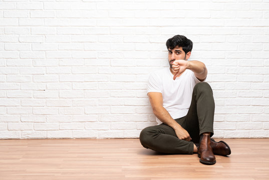 Young man sitting on the floor showing thumb down with negative expression