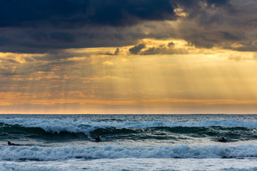 Sufers riding into colorful sunset at Piha Beach, New Zealand