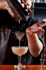 Barman makes a beautiful cocktail at the bar. The barman whipped the cocktail. Blurred bar. Space.