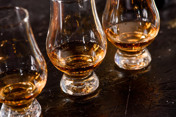 Three Glencairn Glass with whiskey on a bar wooden counter close up on the background of blurry bottles. Close up. Dark background