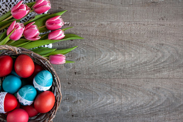  Wielkanocne tło z różowo-białymi tulipanami i koszykiem pełnym kolorowych pisanek ozdobionych...