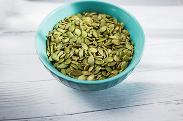 Pumpkin seeds in blue bowl over wooden background close up