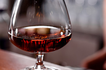 Glass Snifter with cognac on a wooden bar counter in a restaurant close-up. Handsome male drink in...