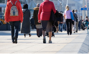 a group of people in coats, jackets, and raincoats is walking along the road. back view