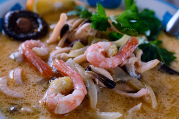 Colorful delicious soup tom yam in a bowl with shrimps, herbs, mushroom and seafoods, macro