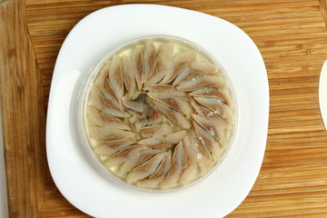 canned russian fish pieces of herring in oil in a jar on a white plate and wooden board  with bread