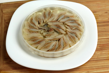 canned russian fish pieces of herring in oil in a jar on a white plate and wooden board  with bread