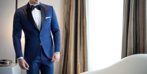 Man model in expensive custom tailored blue tuxedo, suit standing and posing indoors