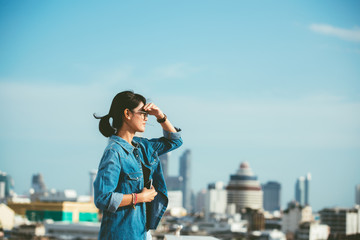 Portrait of a relaxed Asian woman looking forward at the horizon cityscape in the background with her hand on the forehead- copy space
