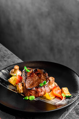 Juicy steak Filet Mignon with grilled vegetables served on a black plate. Mushrooms, zucchini, and sweet peppers are grilled. Close-up. Dark background. Space. Photo for the menu