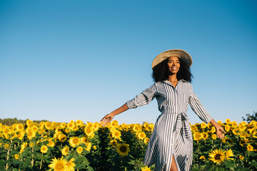 Happy young black woman walking in a sunflower field