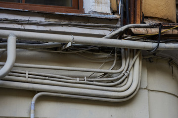 Wires - electrical, telephone, antenna, computer, network on the wall of a dilapidated house with peeling plaster, separate wires in metal pipes with protection