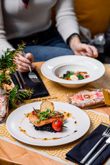 Beautiful serving of roasted salmon fillet and risotto with cuttlefish ink on a white plate with a signature sauce and Cherry tomatoes in a restaurant. close up