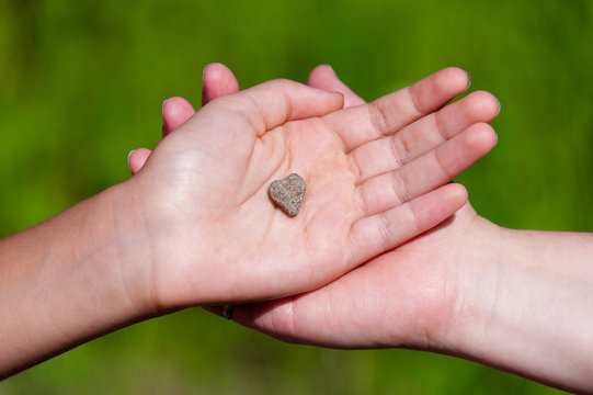 Close up of mother and daughter's hand holding heart shaped rock