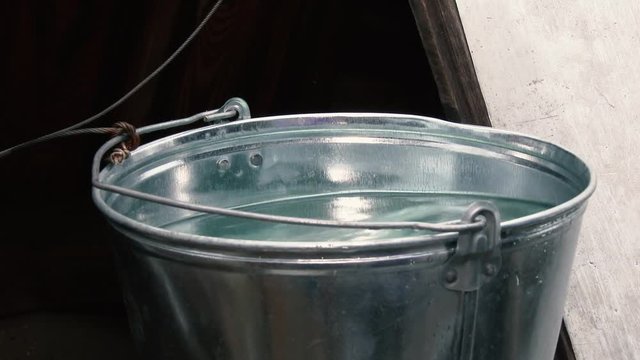 A full metal bucket of water is on the well.