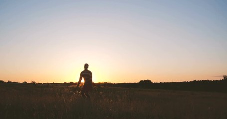 Happy young man jumping and raising his hands at sunset in slow motion
