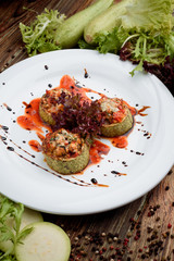 Vegetarian menu. Zucchini slices stuffed with vegetables in tomato sauce on a white plate with lettuce on a dark wooden background. Space. Close-up