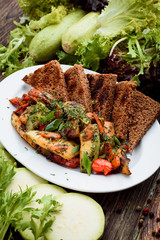 Lenten menu. Grilled vegetables: bell peppers, tomatoes, zucchini, celery on a white plate with dark toast. Plate with grilled vegetables on a wooden rustic background among greens. Close-up. Space