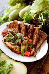 Lenten menu. Grilled vegetables: bell peppers, tomatoes, zucchini, celery on a white plate with dark toast. Plate with grilled vegetables on a wooden rustic background among greens. Close-up. Space