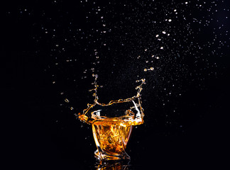 whiskey with splash on black background, brandy in a glass