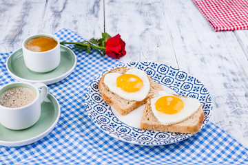 Two cups of aromatic coffee and heart-shaped toasts for a romantic morning of lovers. Red rose and morning surprise for breakfast. The concept of Valentine's Day and Mother's Day. Copy space. 