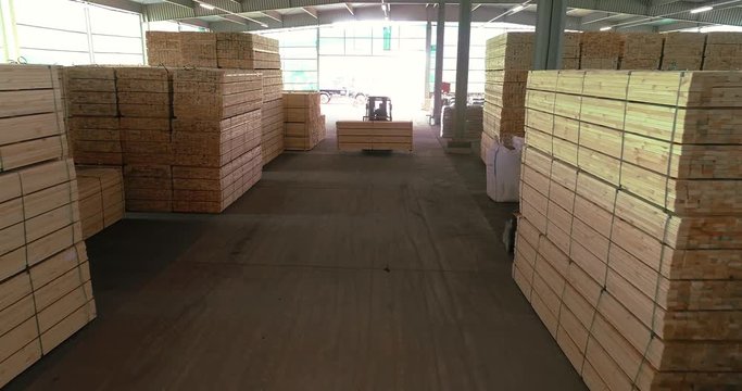 A forklift carries a wooden beam through the sawmill's warehouse. Modern warehouse sawmill. A large warehouse of timber materials. Neatly stacked wooden bar in a sawmill warehouse