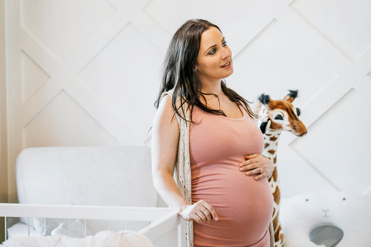 Pregnant woman standing near crib at home