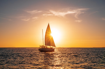 Sailing yacht in the ocean at sunset - obrazy, fototapety, plakaty