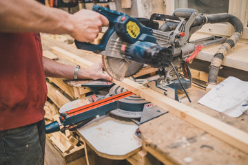 A craftsman cuts a wooden block on an electric circular machine