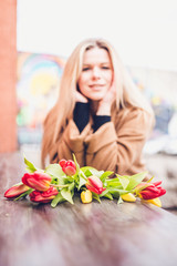 Obraz na płótnie Canvas Portrait of a girl of good appearance with thick blond hair on a background of a bouquet of tulips - out of focus, selective focus, blur