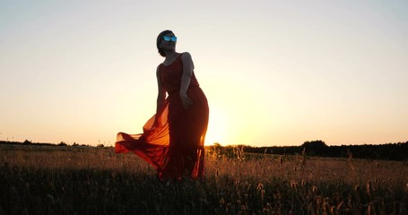 Cheery elegant woman in a red dress dancing in a field at sunset in slow motion